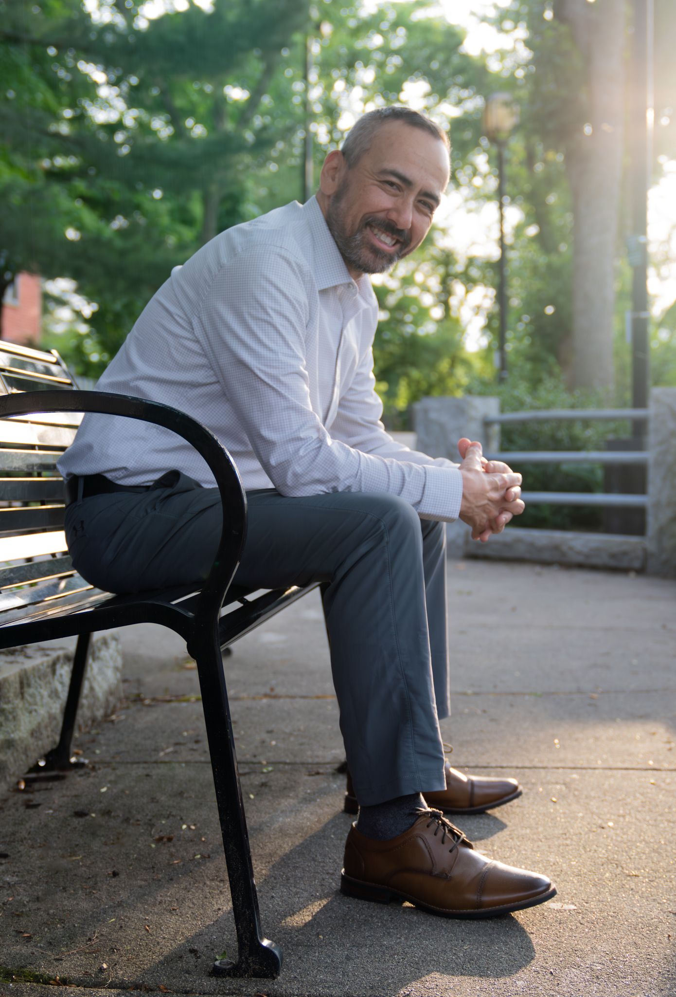 Person in business attire sitting on park bench during golden hour.