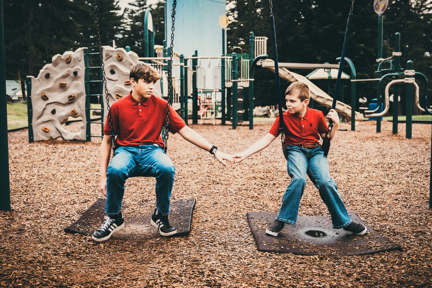 Children in matching red shirts playing on mulch-covered playground.