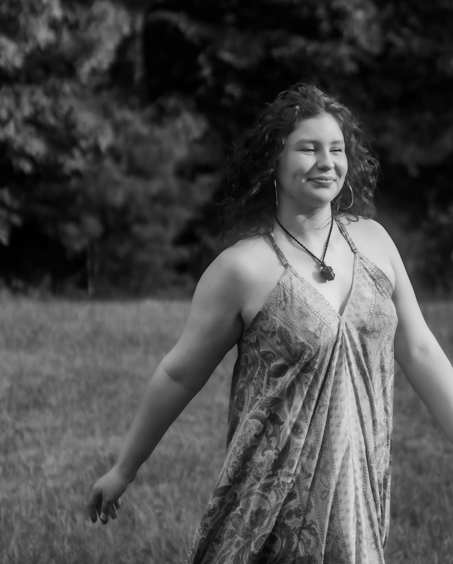 A joyful person in a floral dress spins and dances in a grassy field on a sunny day.