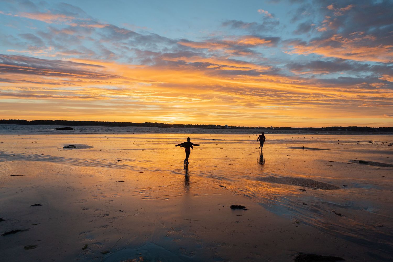 Dramatic sunset over a beach with silhouetted figures walking along the shoreline.