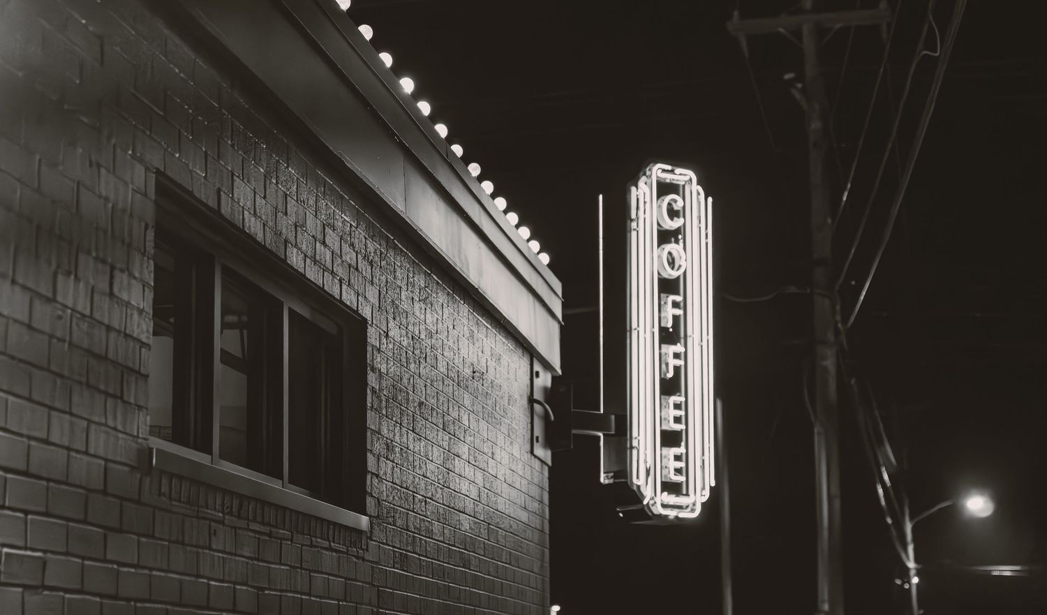 Moody black and white urban alley with brick walls and utility poles at night.
