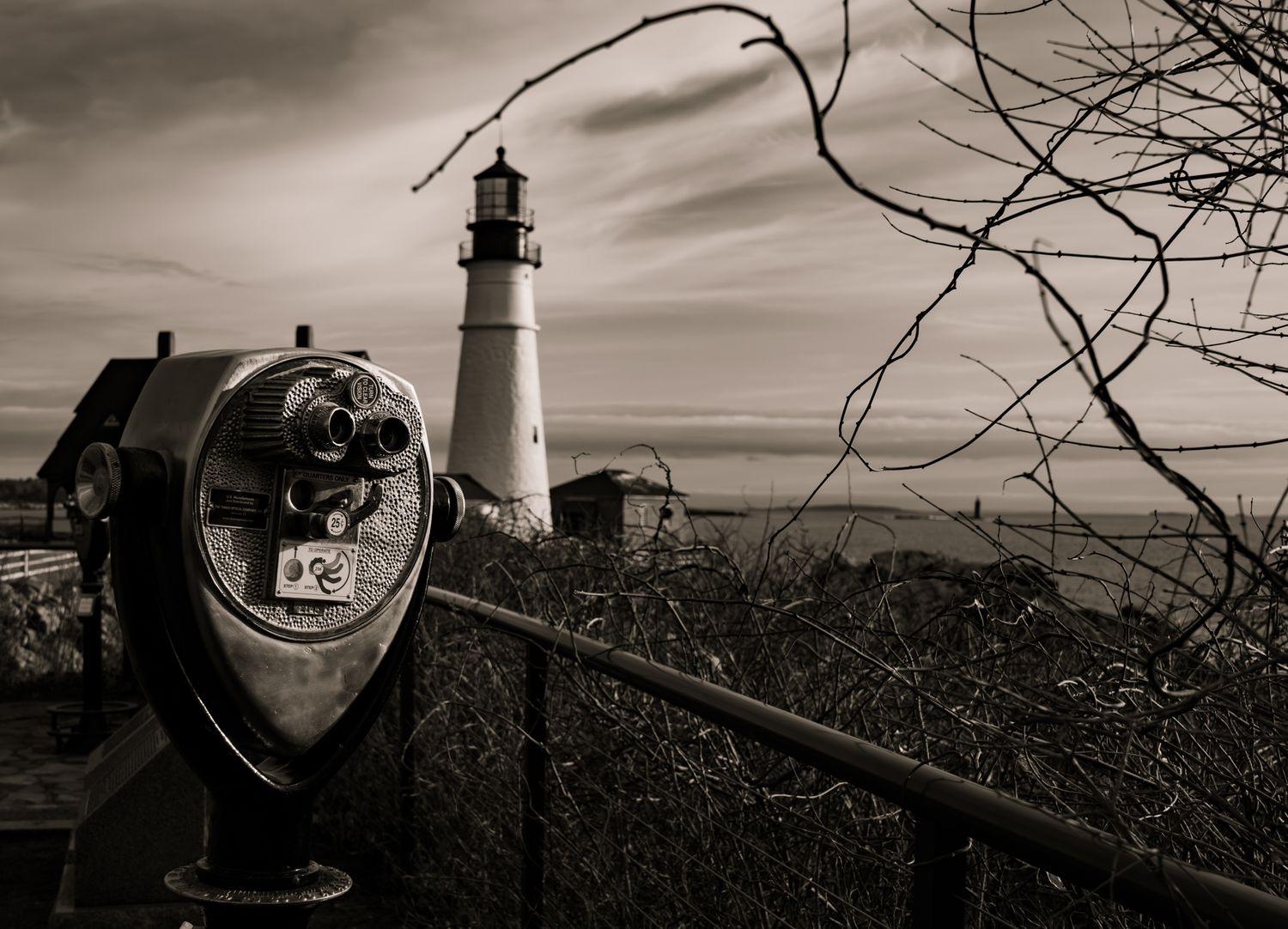 Black and white panorama of Portland Head Light lighthouse with vintage binoculars in foreground.