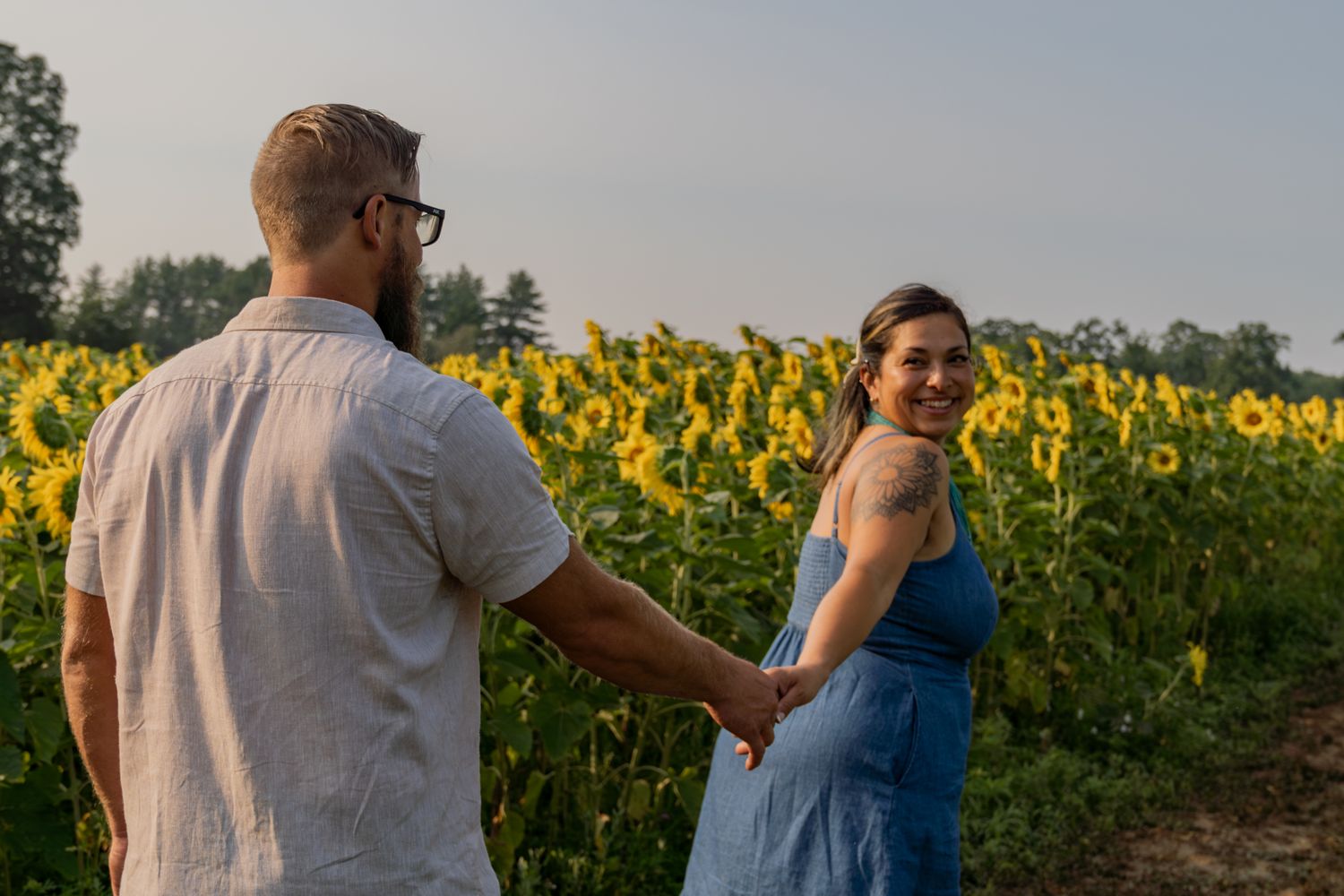 A couple poses playfully in a blooming sunflower field during golden hour.