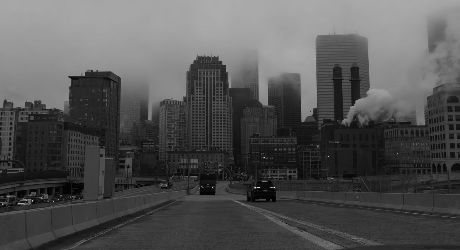 Black and white cityscape showing foggy urban skyline with bridge in foreground.