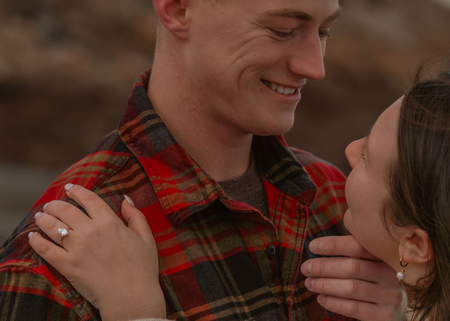 Romantic couple embracing in plaid flannel during sunset moment.