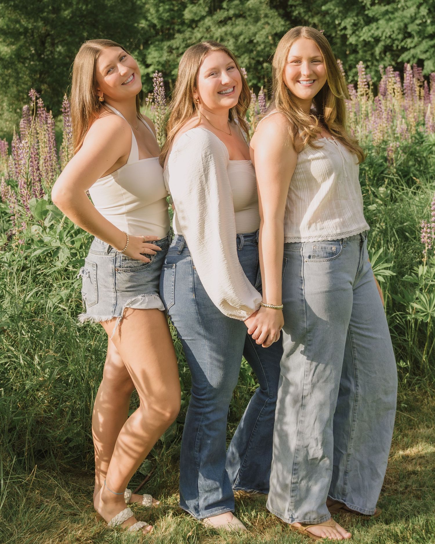 Sisters in matching white tops and denim posing together in a garden setting.