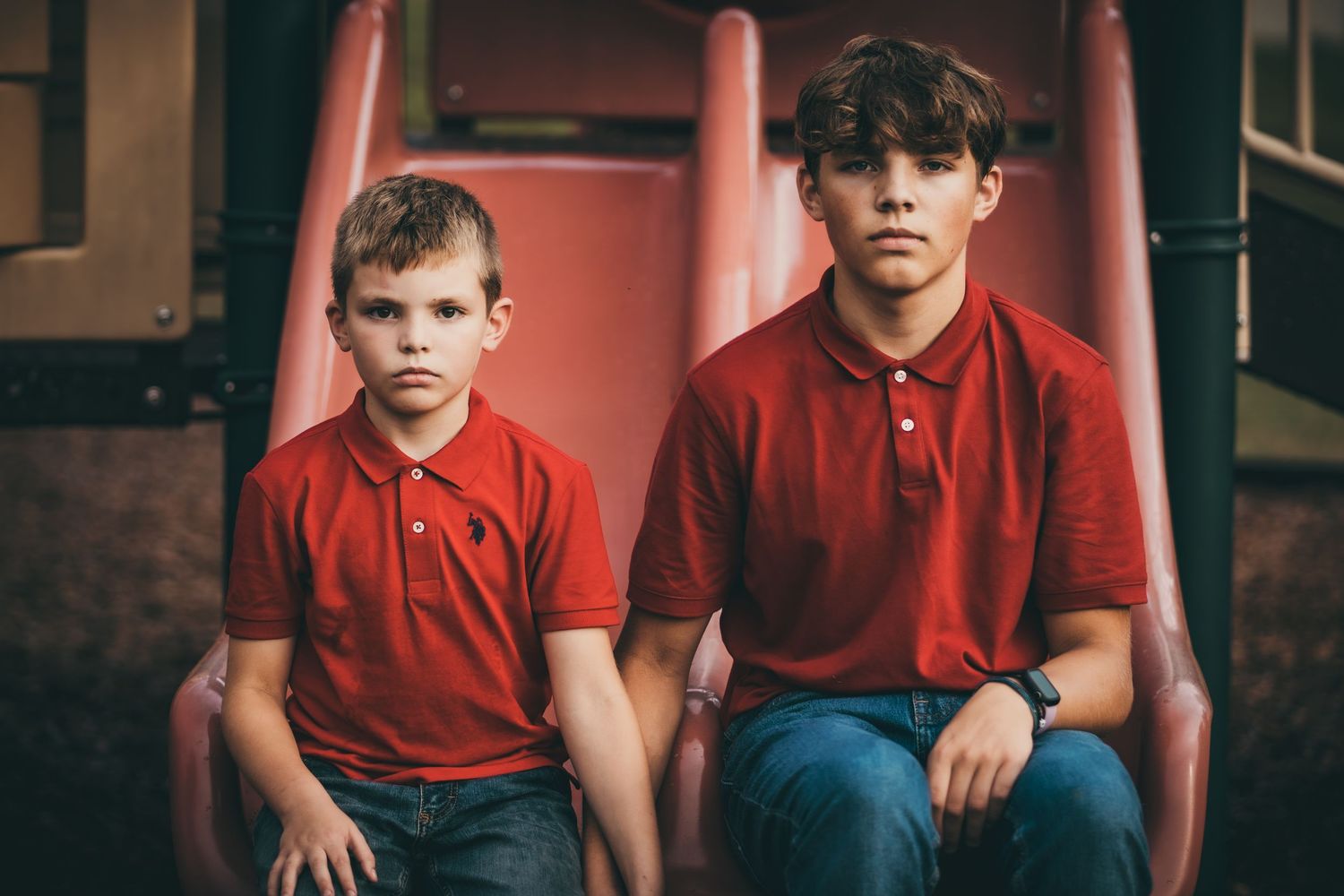 People wearing matching red shirts sit together on a pink playground seat.