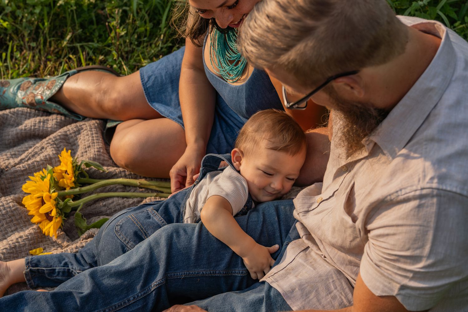 Family enjoying a sunset picnic with sunflowers on a blanket in warm golden light.
