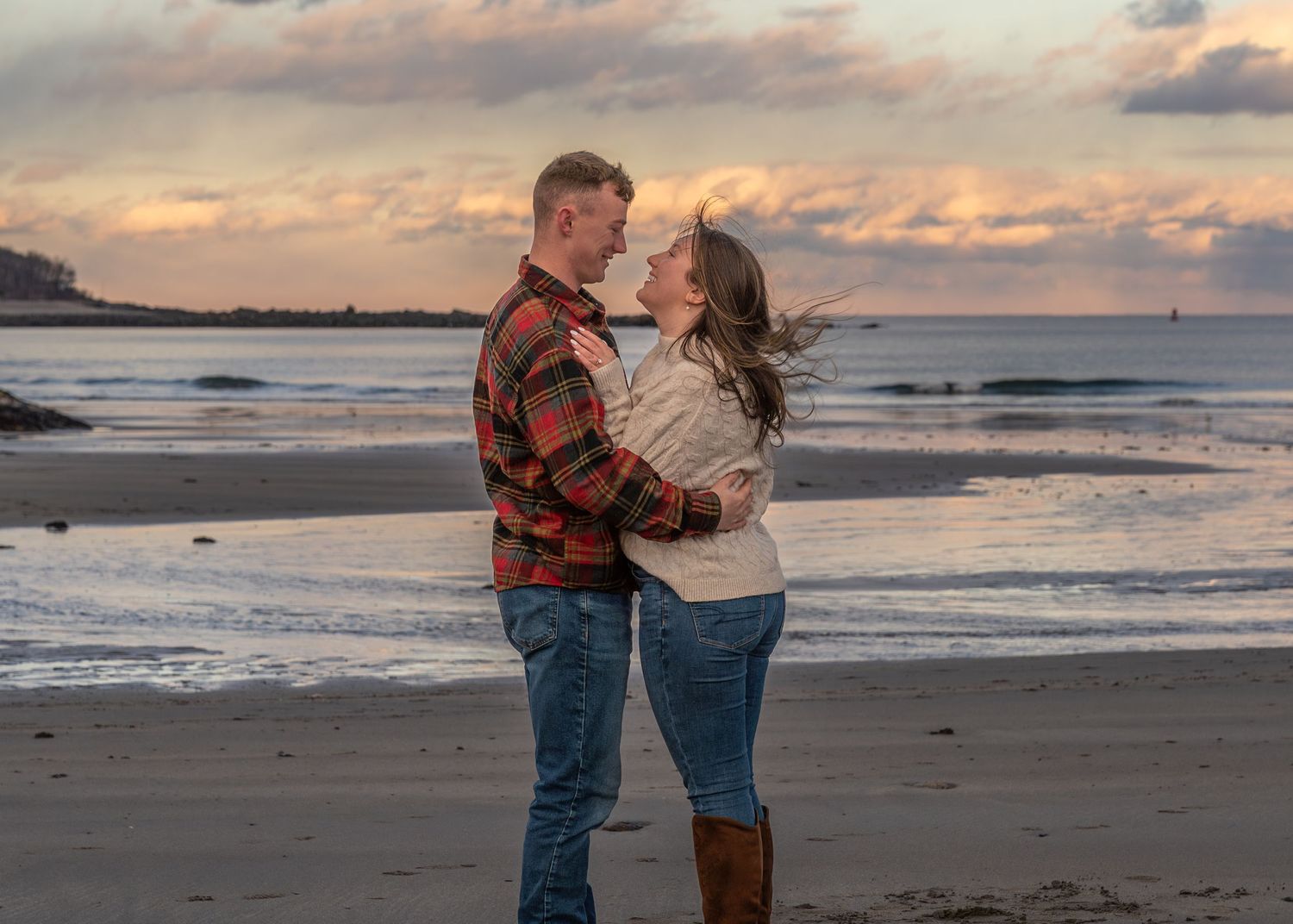 A couple shares intimate moments on a beach at sunset with waves crashing behind them.