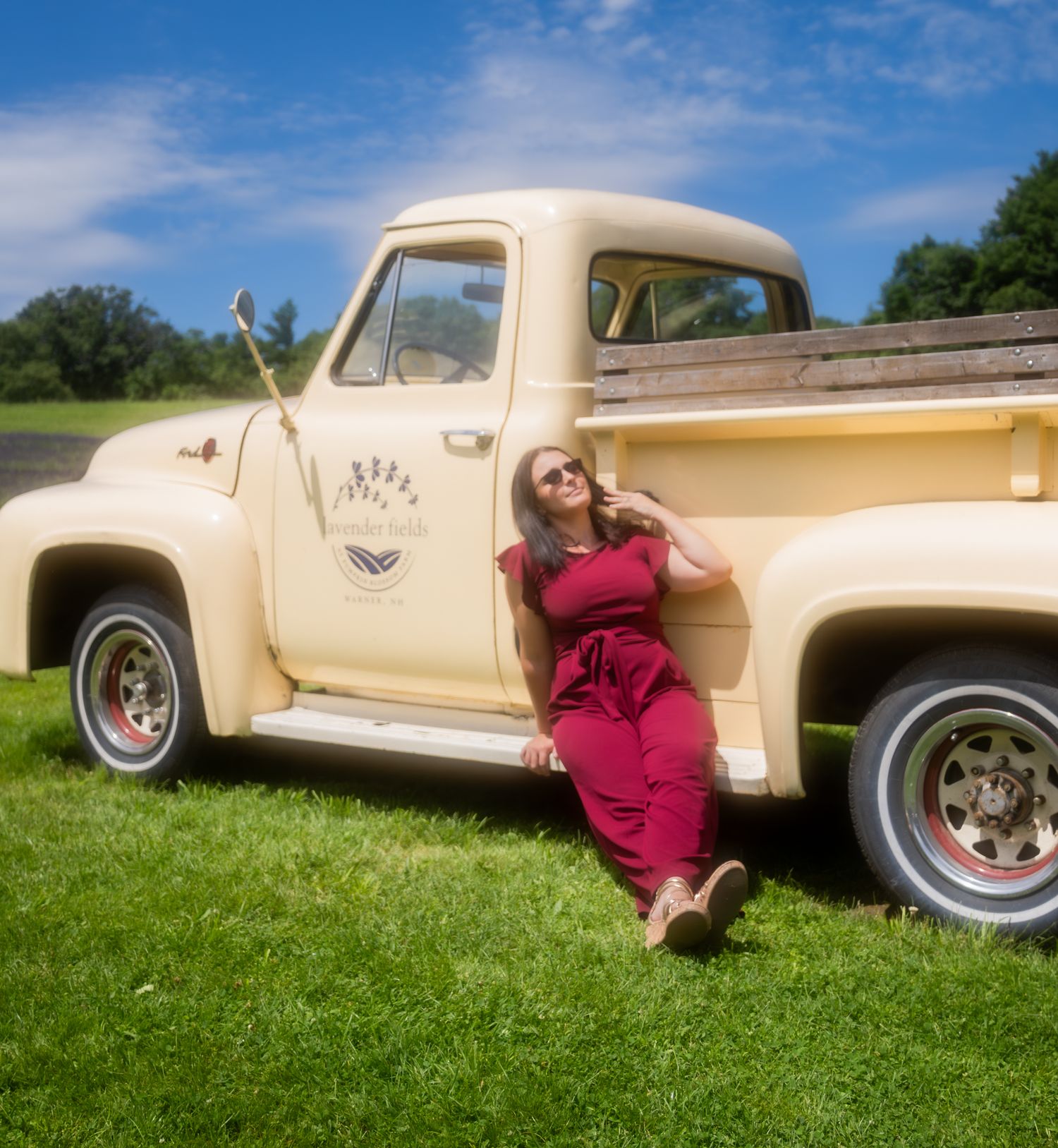 A classic cream-colored vintage car sits on lush green grass under blue skies.