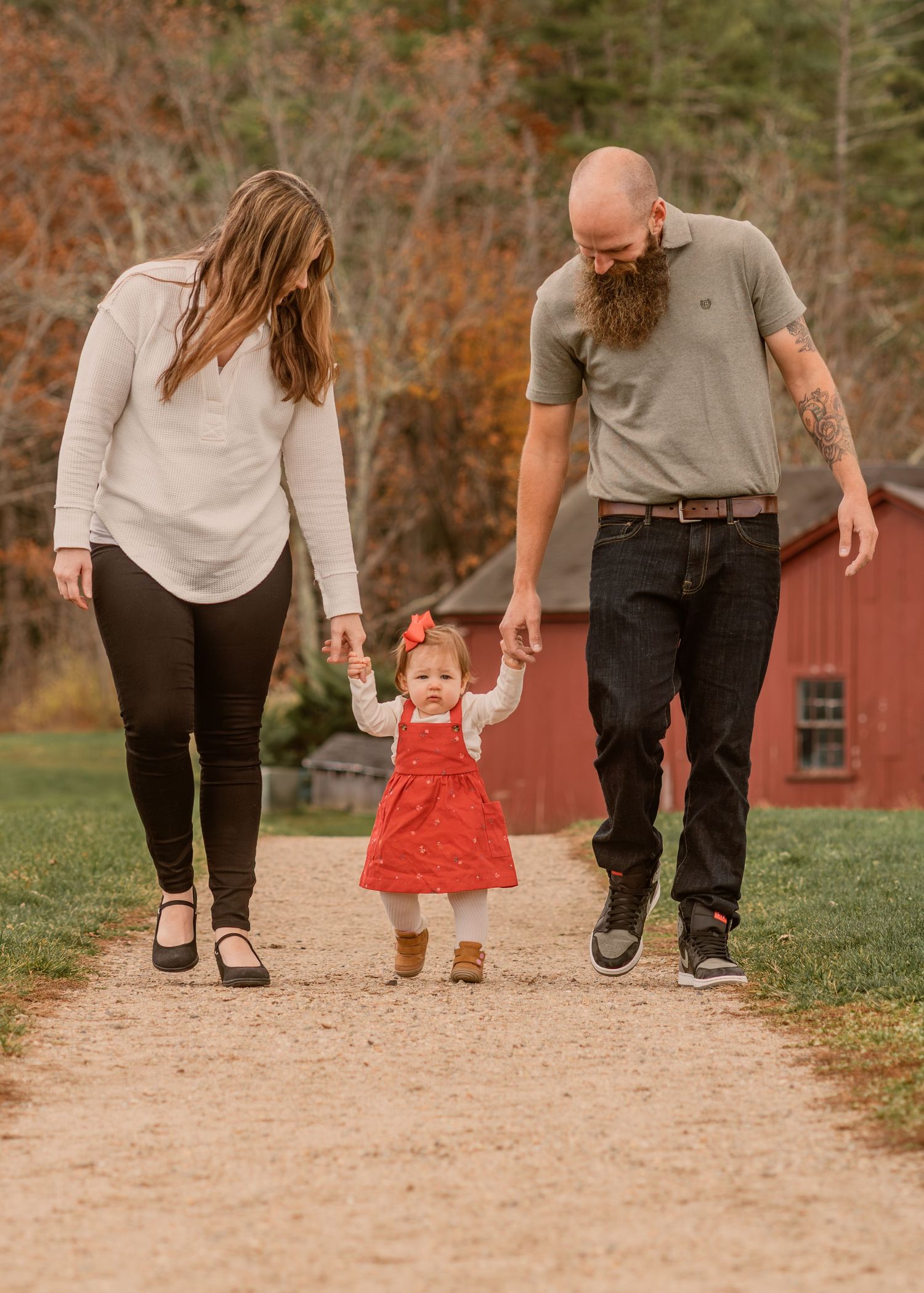 A family walks together on a dirt path with a red barn in the background.