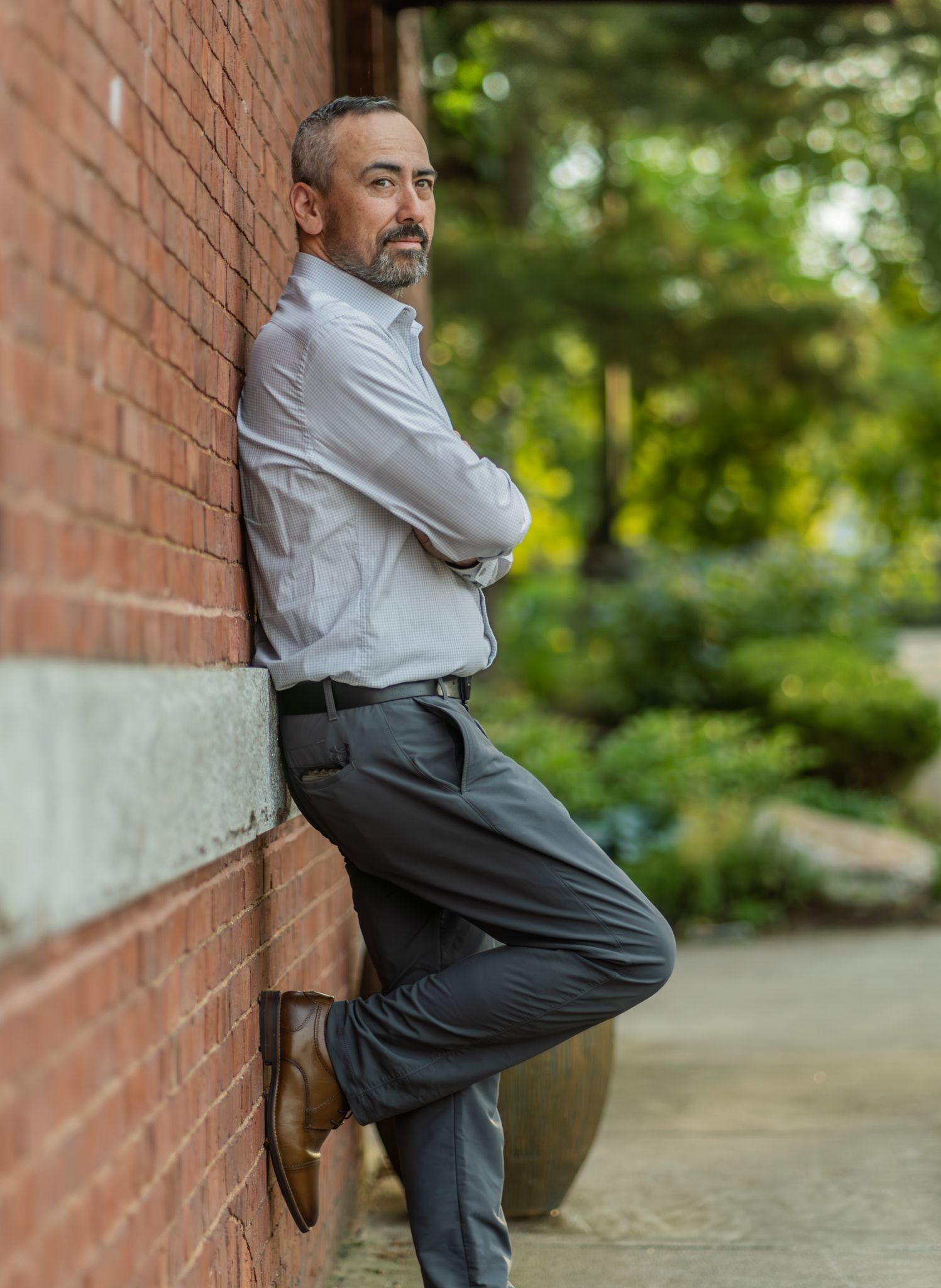 Professional leaning against brick wall in business attire showing confident pose.