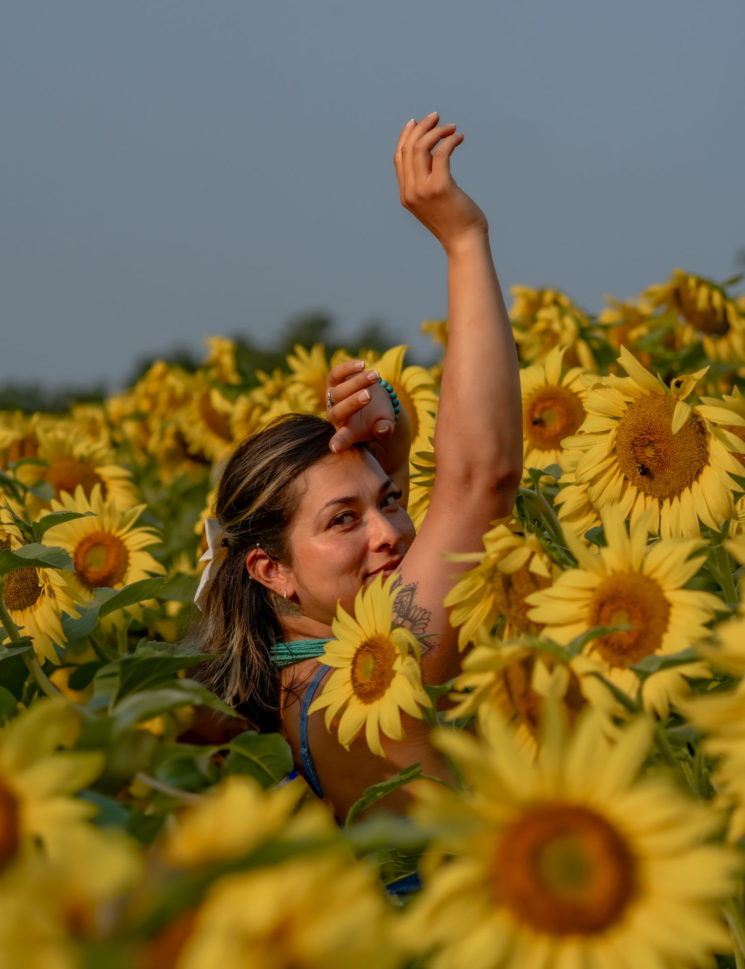 A woman posing playfully in a vibrant yellow sunflower field on a sunny day.