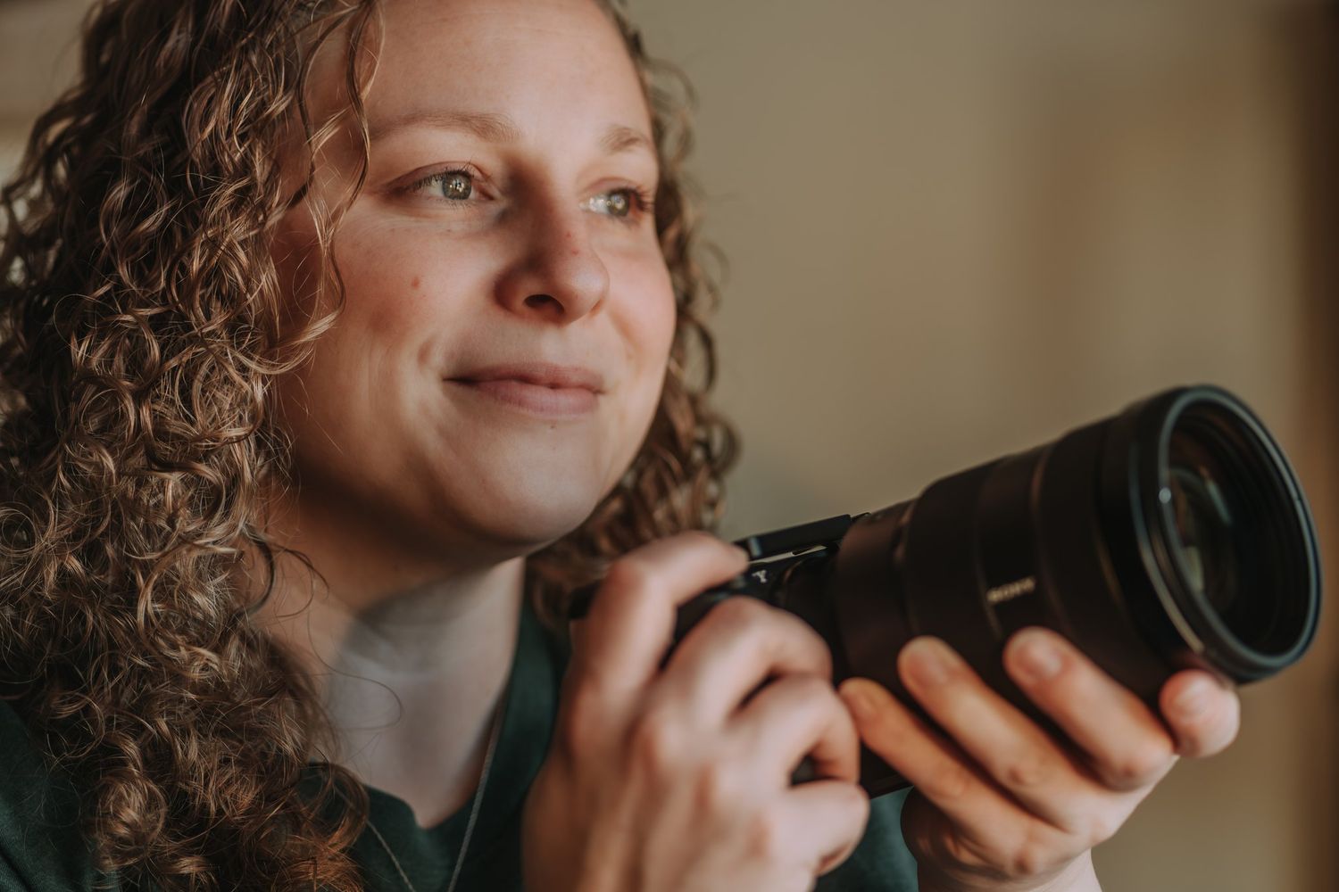 Woman with curly hair holding a camera and smiling while taking photos in natural light.