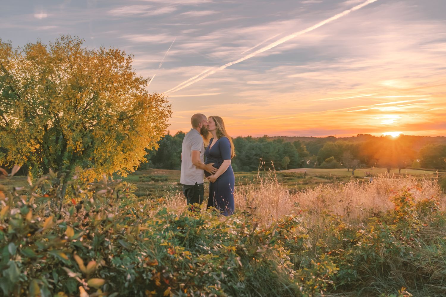 Panoramic sunset landscape with golden light illuminating a couple in a natural field setting.