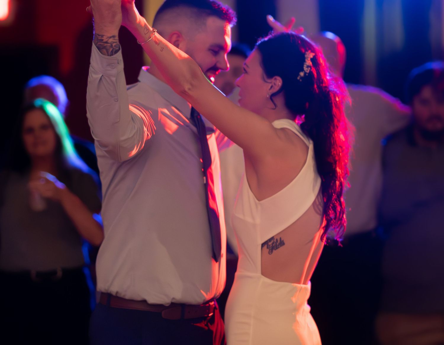 Couple dances together under colorful party lights at wedding reception.
