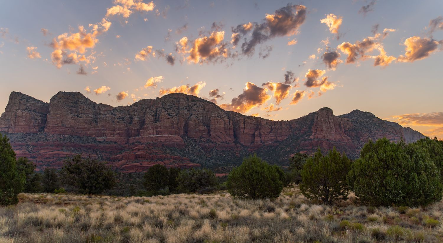 Dramatic sunset clouds glow orange over silhouetted desert mountain landscape.