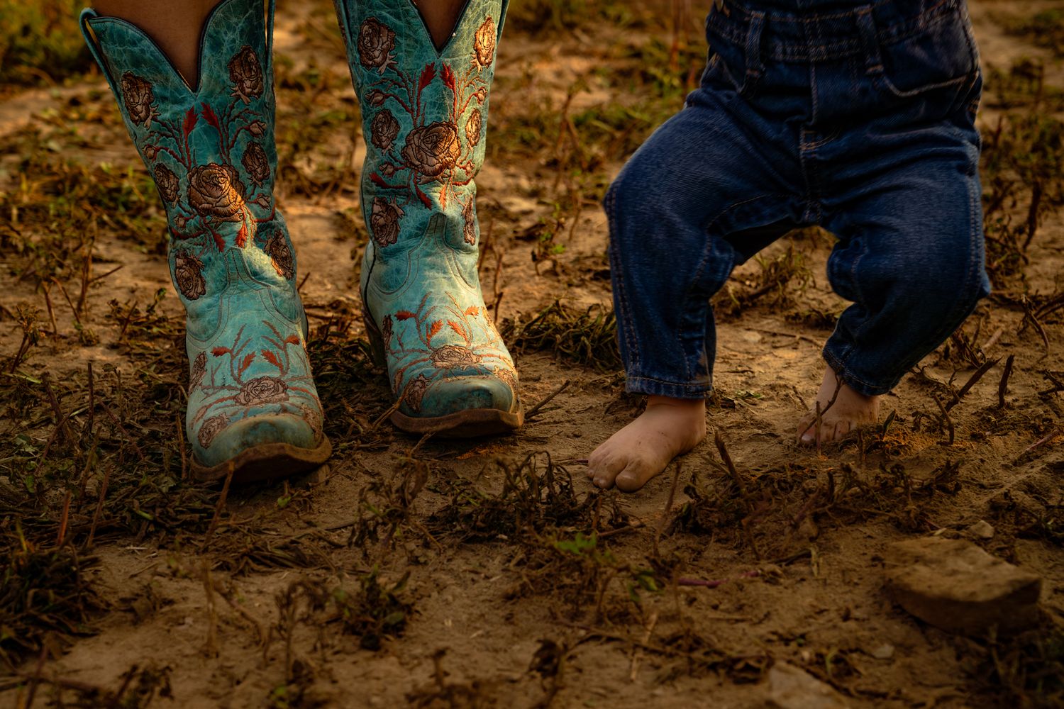Row of muddy boots and bare feet standing in dirt showing farming or gardening activity.