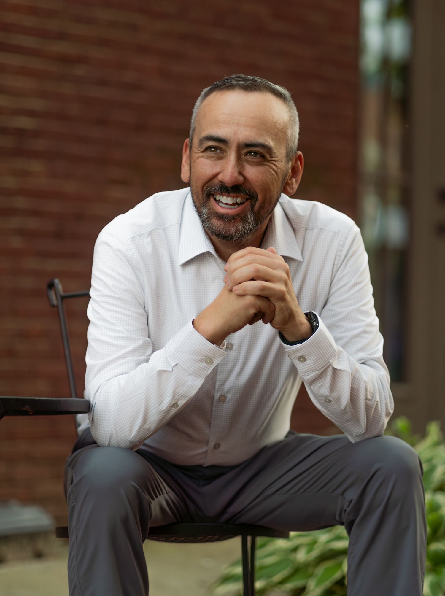 Professional portrait of person in white dress shirt sitting outdoors with warm smile.