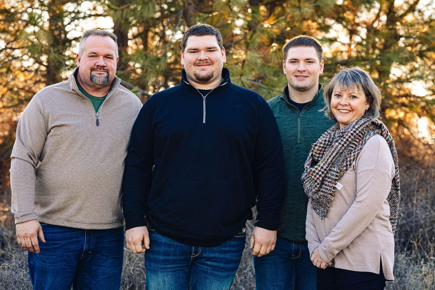 A group of people wearing casual attire pose together outdoors during golden hour sunset lighting.