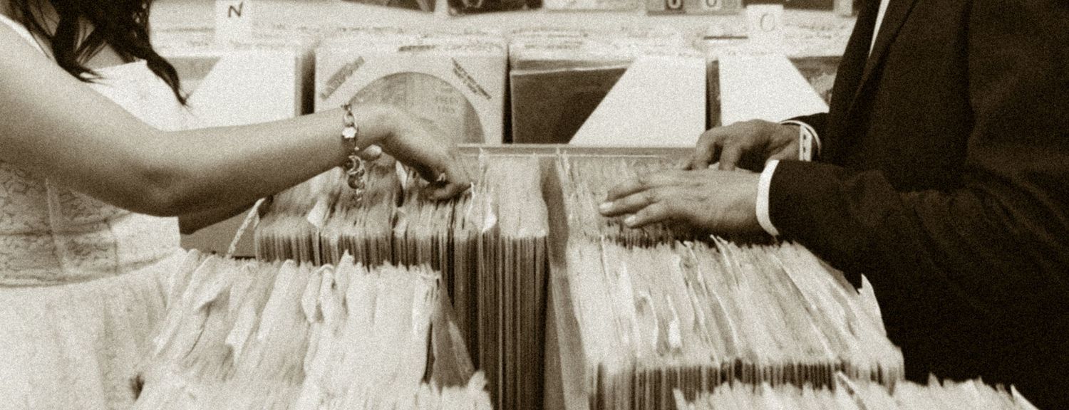 Couple holding hands over a vintage vinyl record collection in sepia tone.