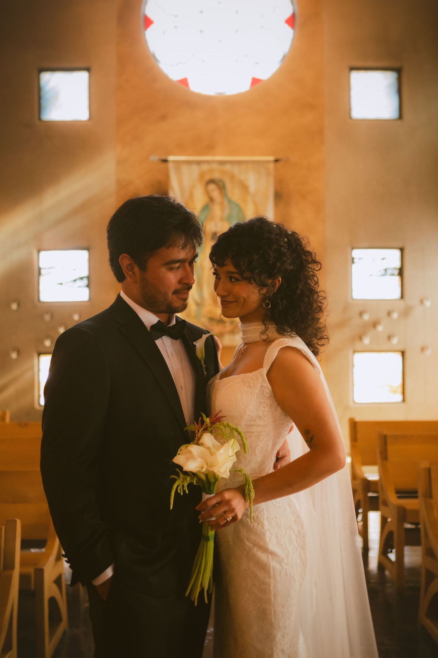 Bride and groom share a romantic moment inside a warmly lit chapel with stained glass windows.