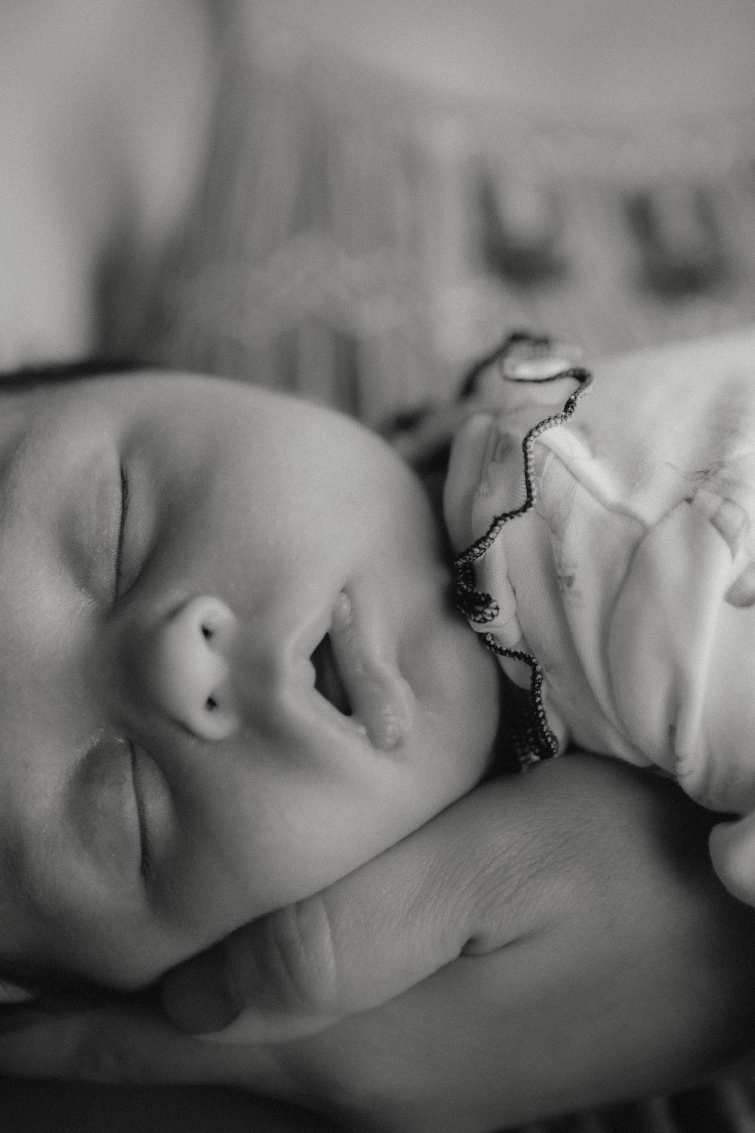 Black and white close-up of sleeping newborn baby face with tiny fist near chin.