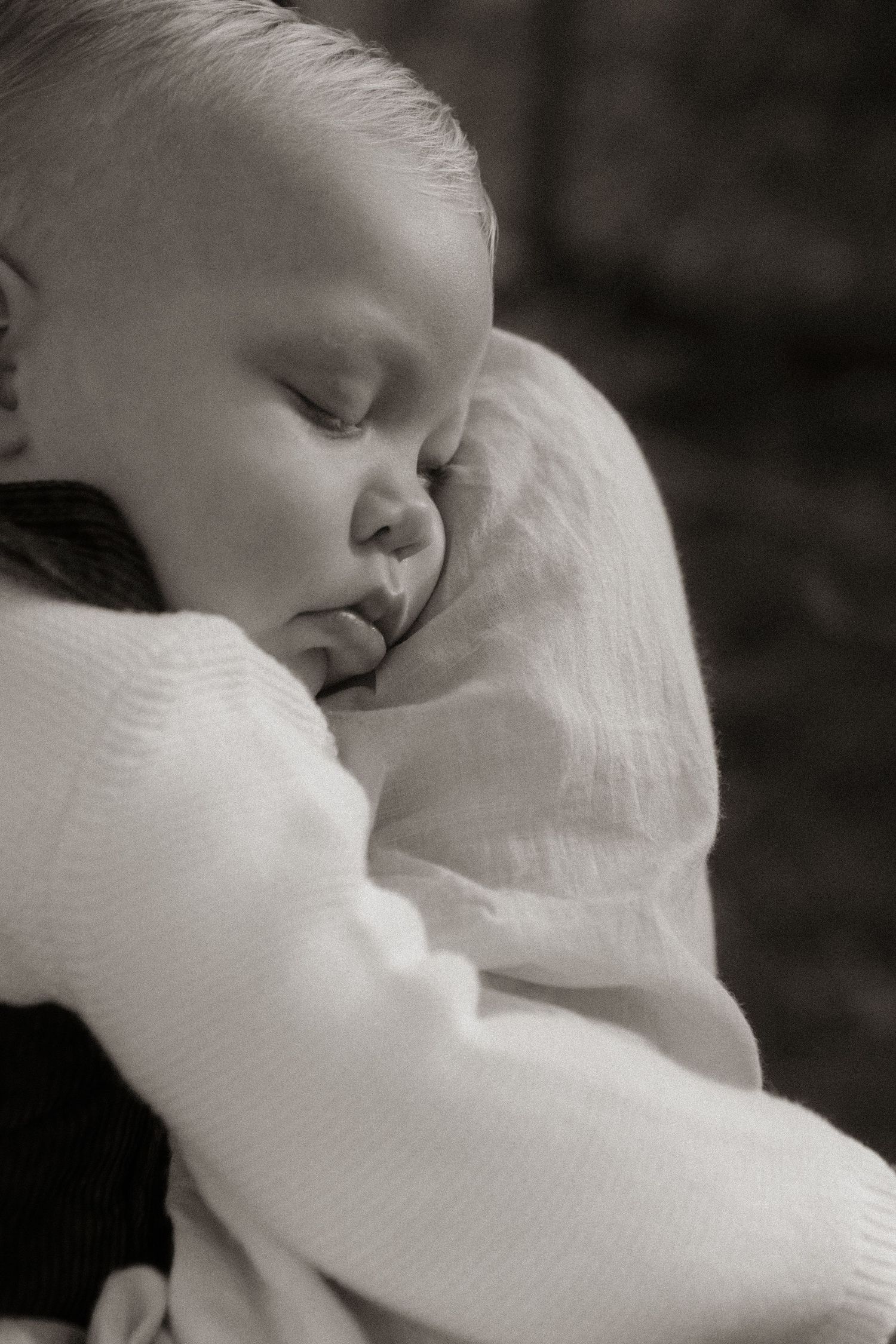 Peaceful sleeping newborn baby wrapped in soft white knit blanket, held in loving arms, black and white portrait.