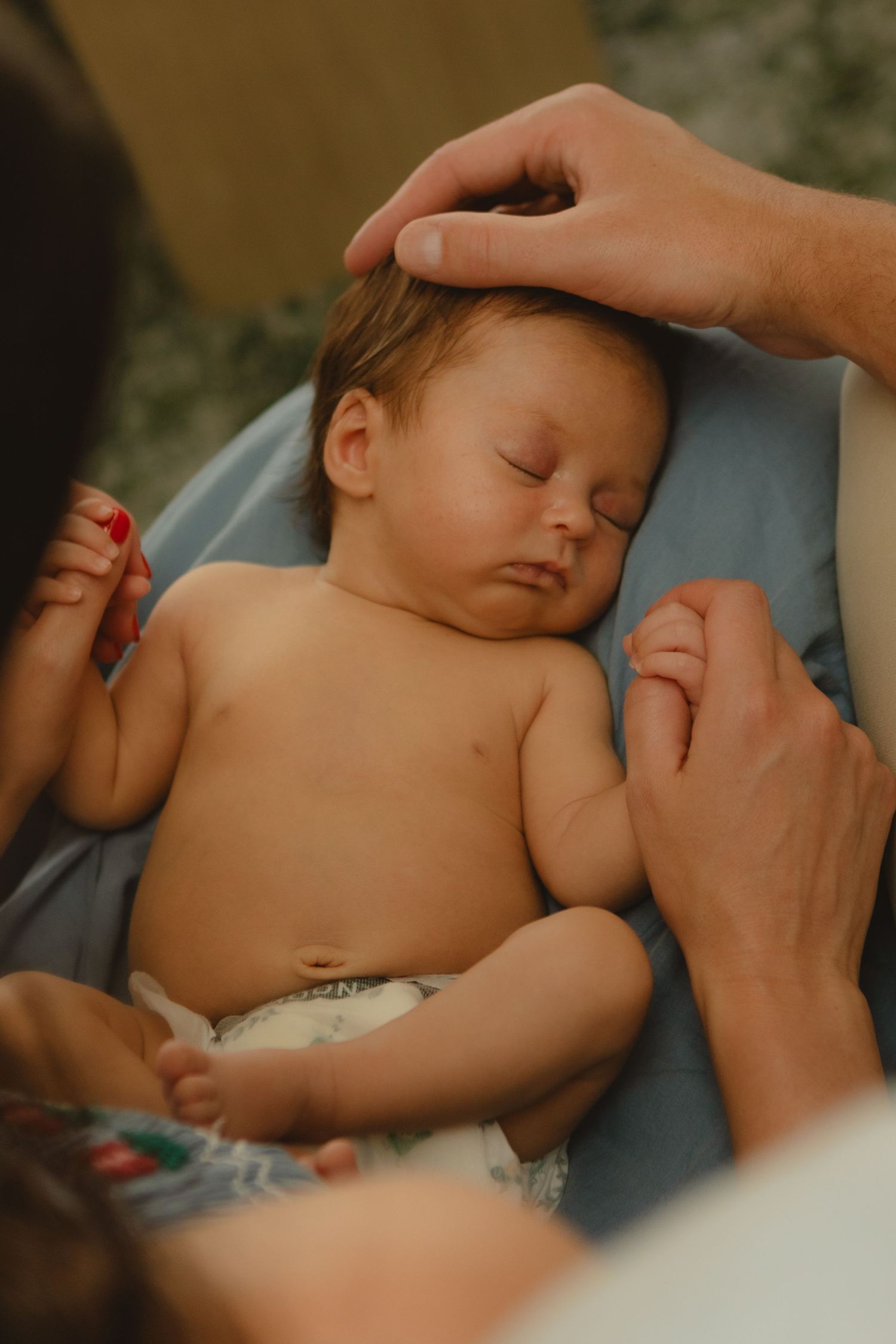 Sleeping newborn baby in diaper cradled by parents' hands in warm natural light.