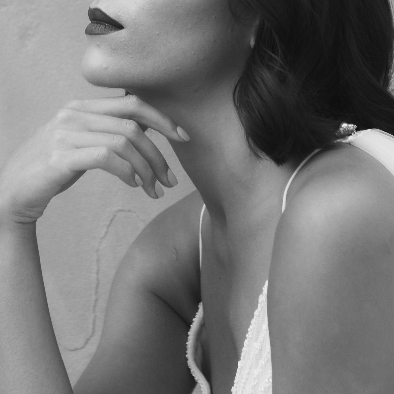 An elegant black and white close-up portrait of a woman in a white dress touching her chin.