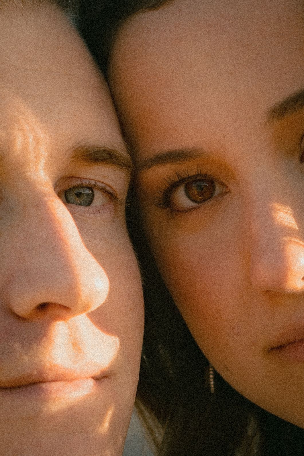 Close-up portrait of two women faces side by side in warm golden sunlight photography.