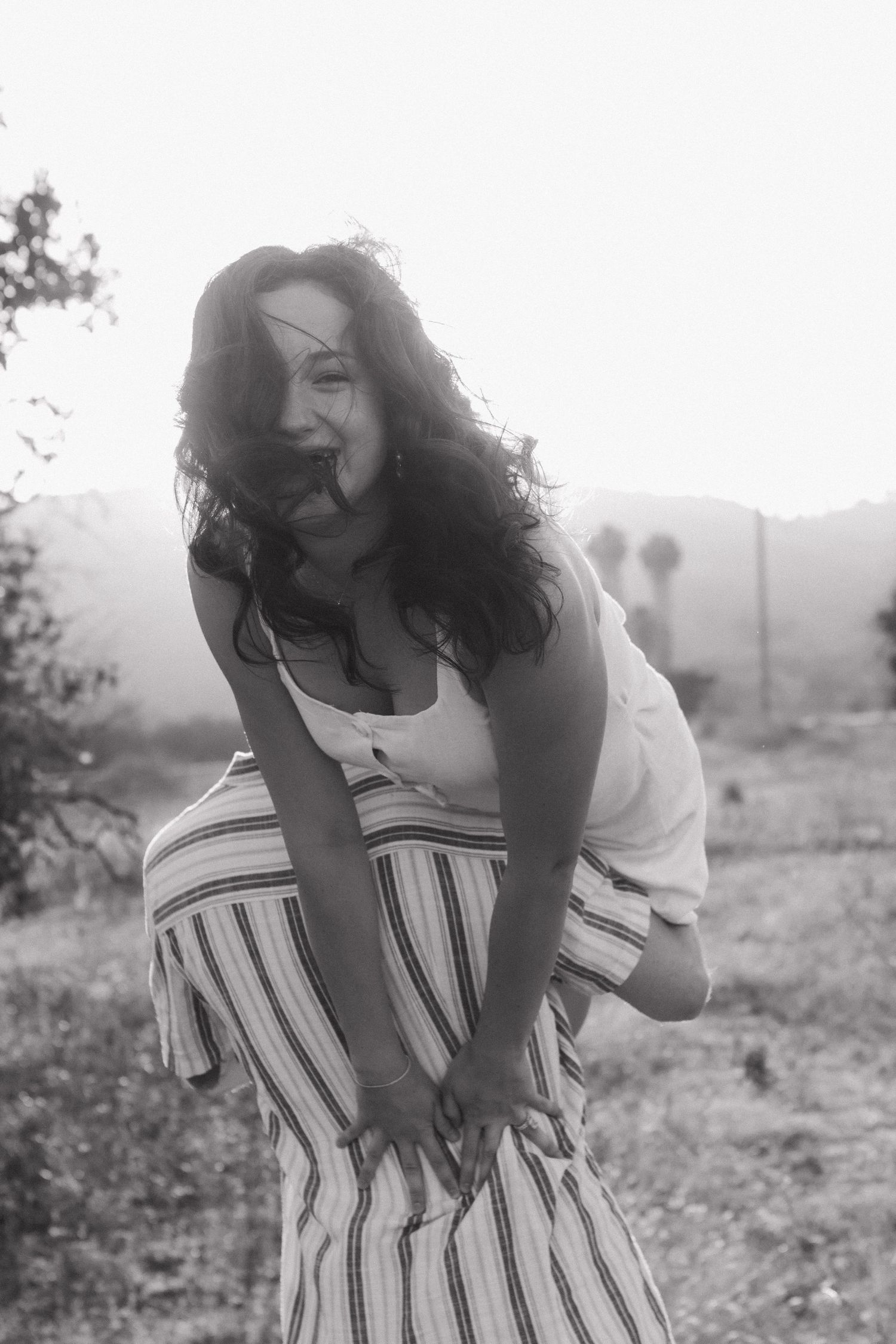 Laughing brunette woman in striped skirt and white top posing outdoors in black and white.