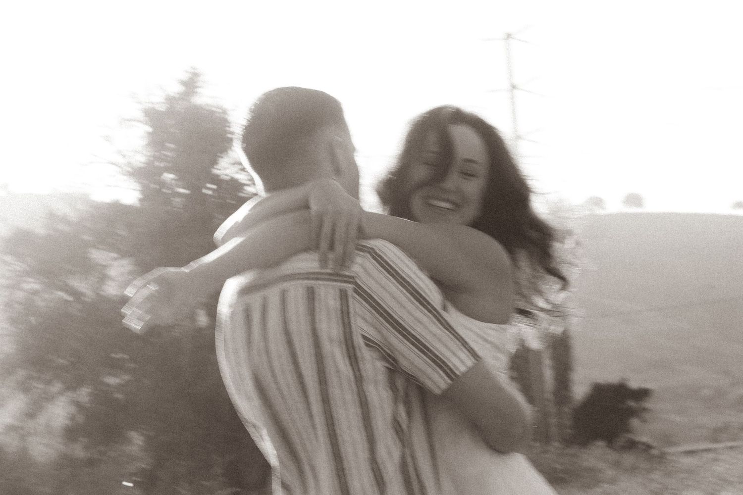 Joyful couple embracing and spinning outdoors in a dreamy black and white romantic photograph.
