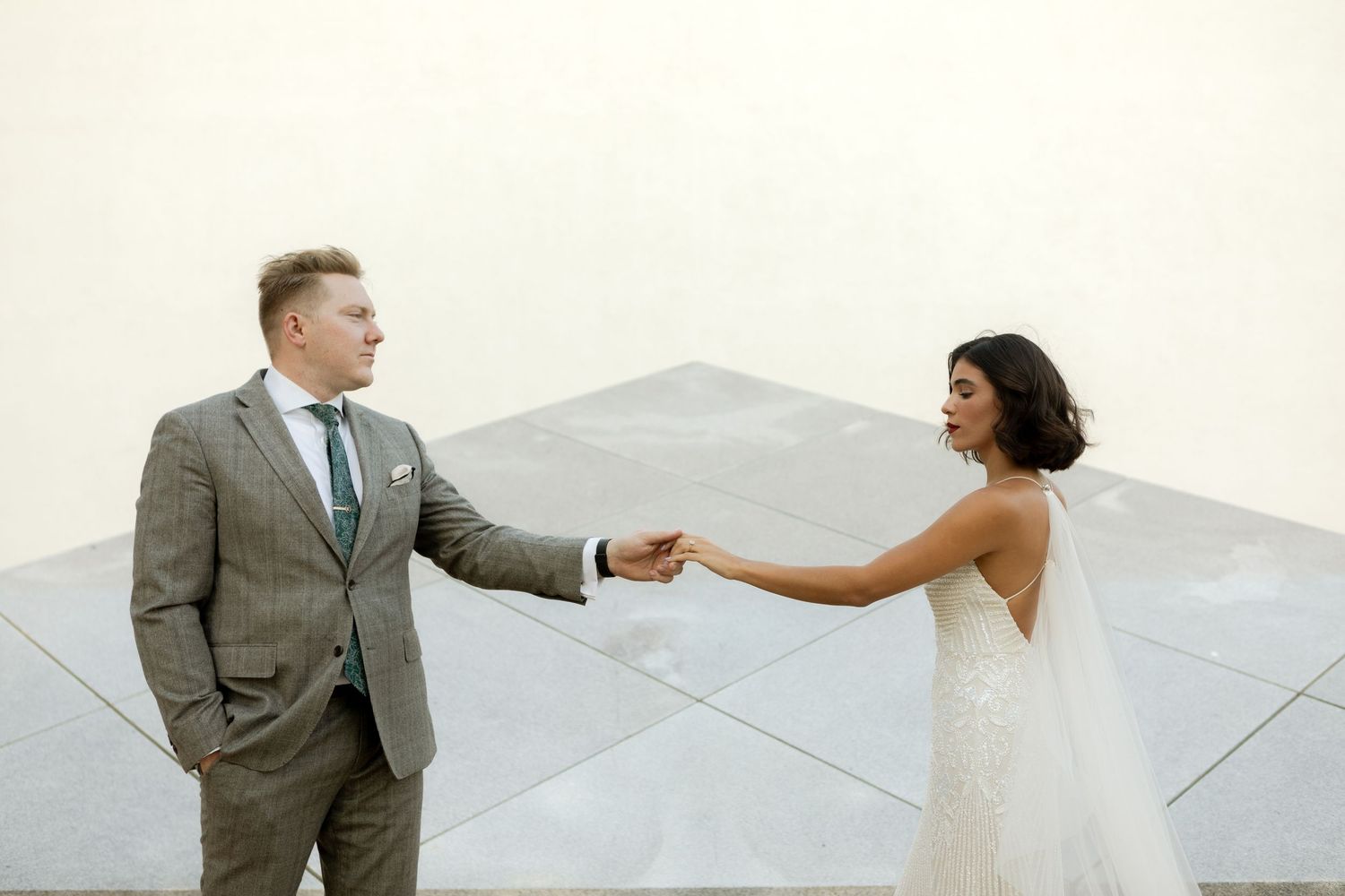Bride and groom hold hands during first look at modern wedding venue.