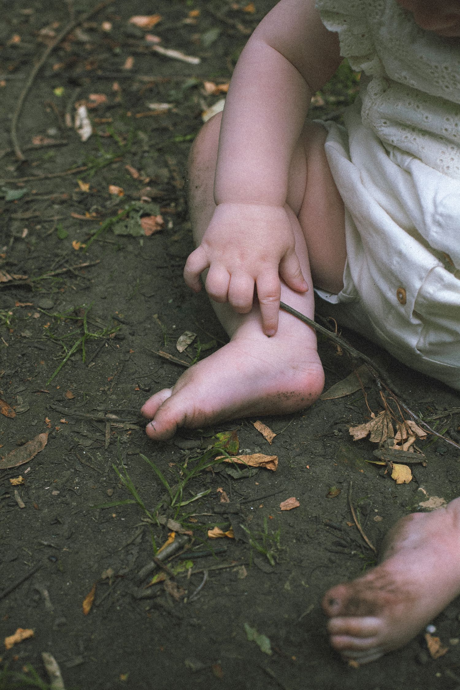 Close-up view of small bare feet on dark ground with scattered leaves.