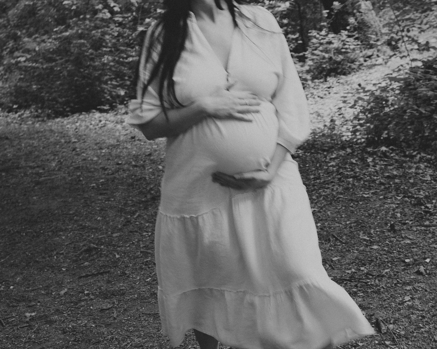 Black and white maternity photo showing a pregnant woman in a flowing dress outdoors.