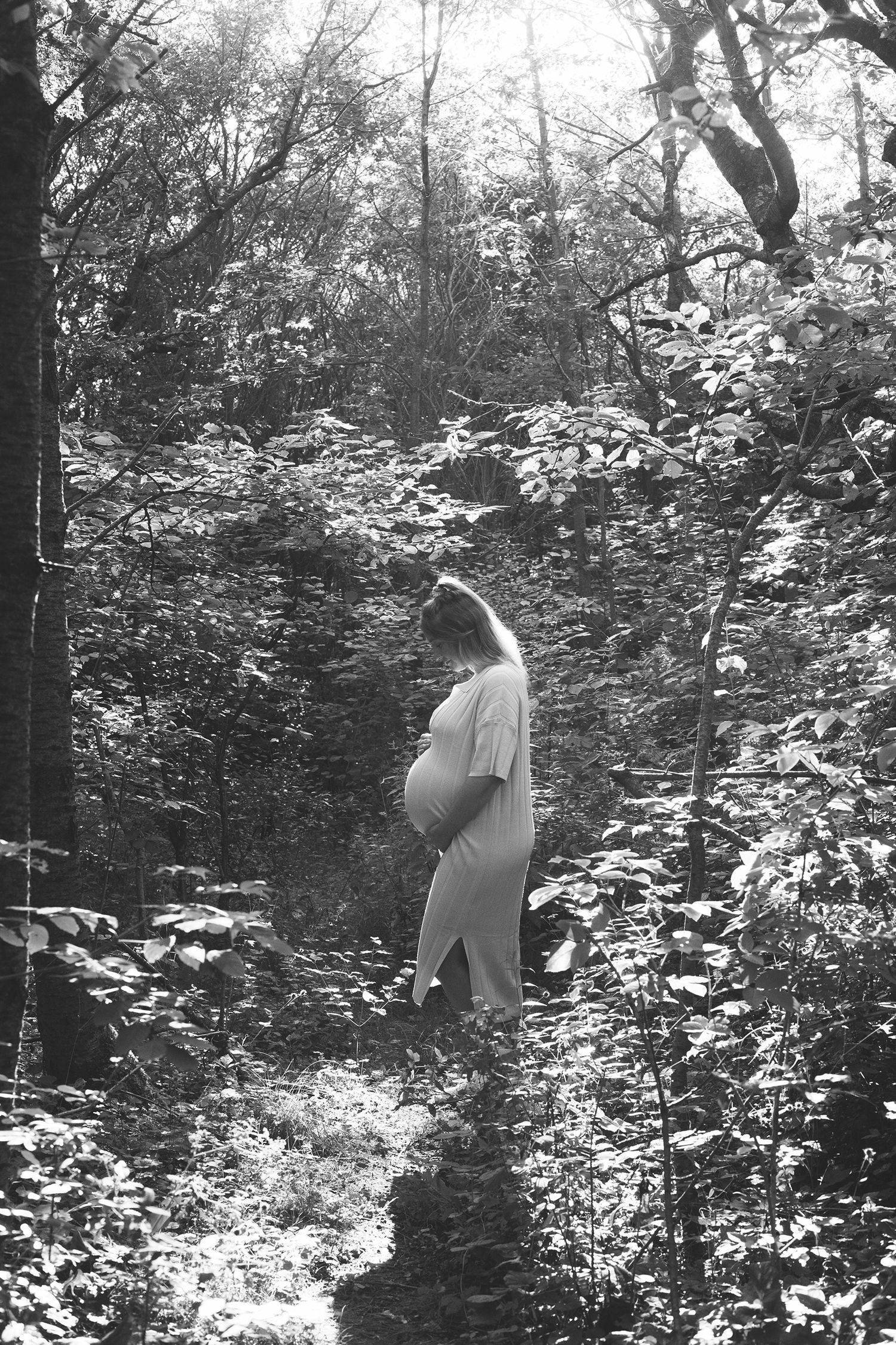 Black and white image of someone walking through a wooded area with dappled sunlight.