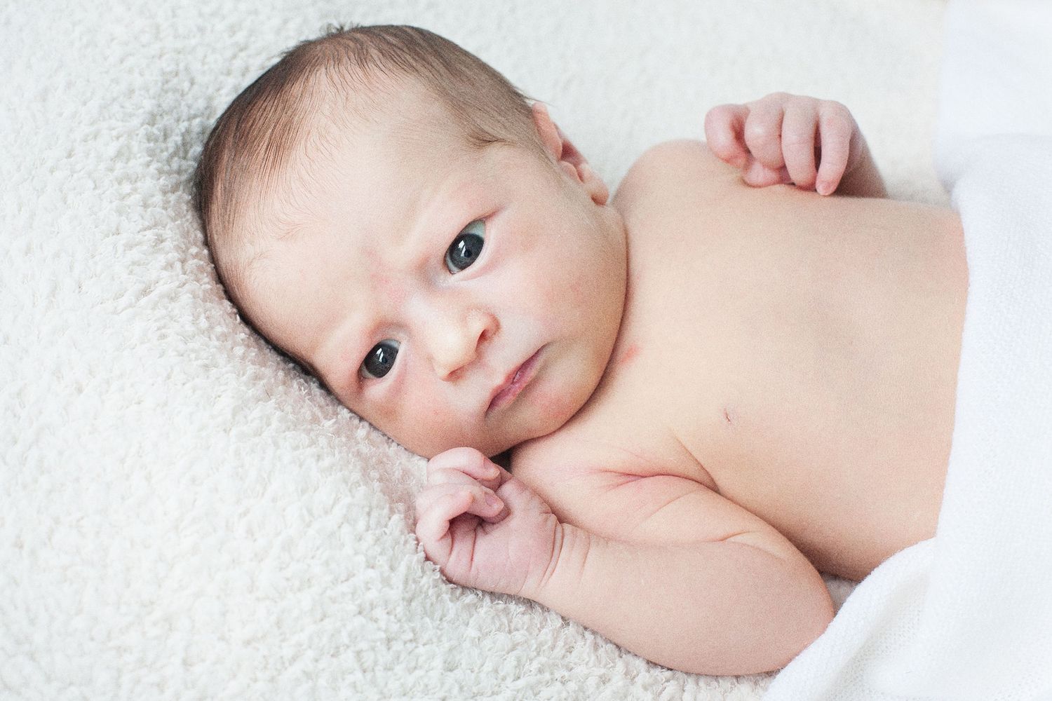 Black and white portrait of a newborn baby lying on soft white fabric.