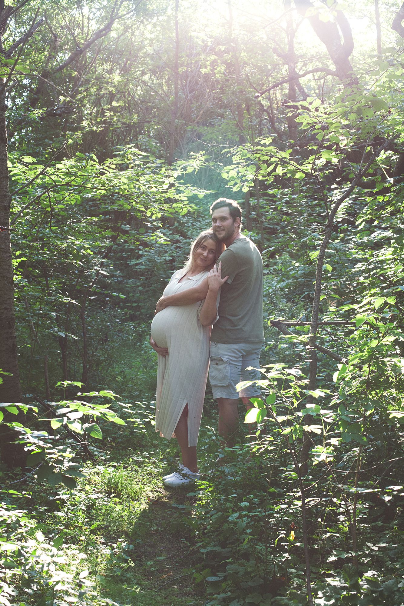 Romantic couple's portrait in a sunlit wooded area with lush greenery.