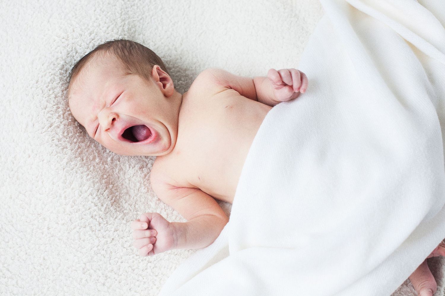 Sweet moment of newborn yawning while wrapped in white blanket.