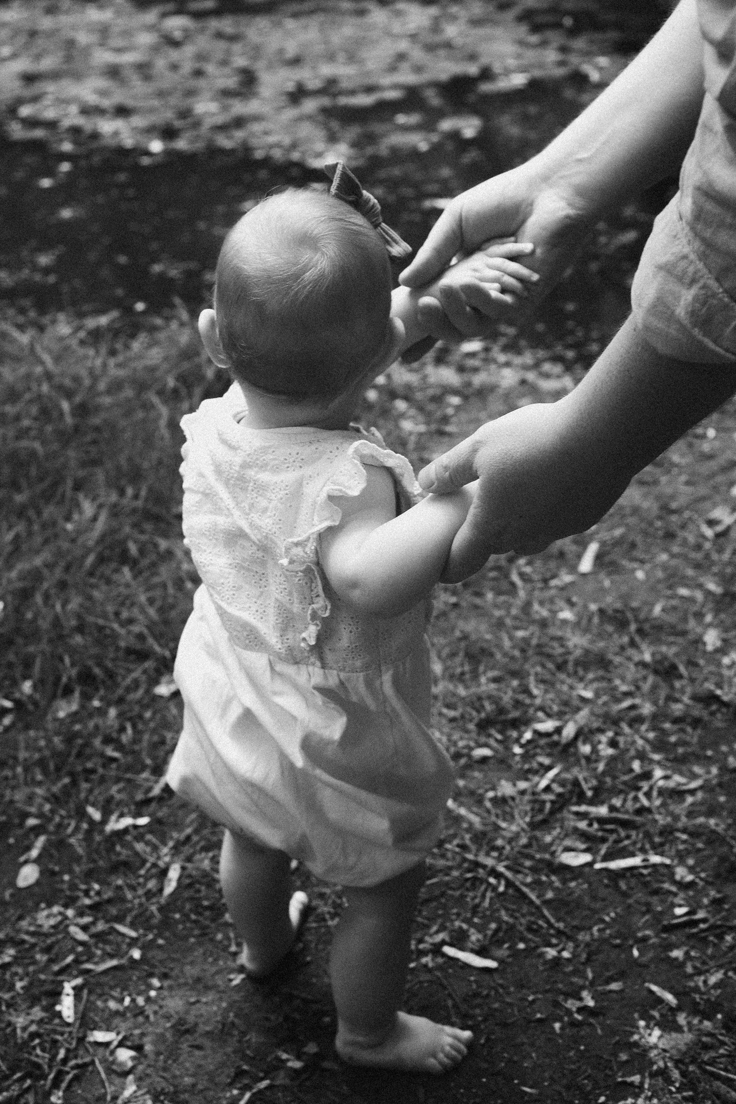 Black and white sequence of someone helping a baby stand on outdoor ground.