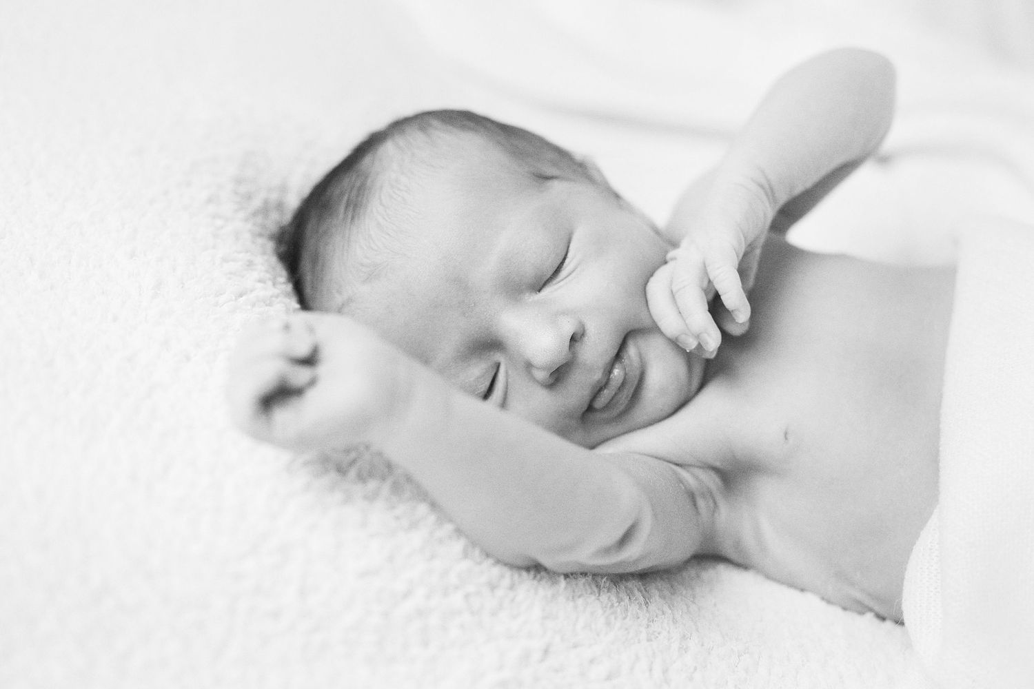 Artistic black and white photo of resting newborn on white textured surface.