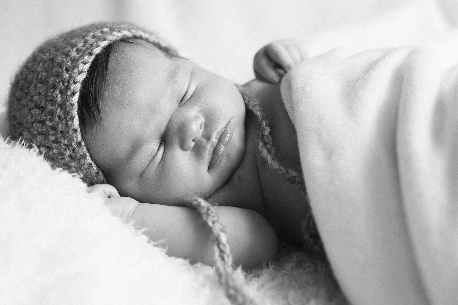 Black and white image of sleeping baby wearing knitted cap.