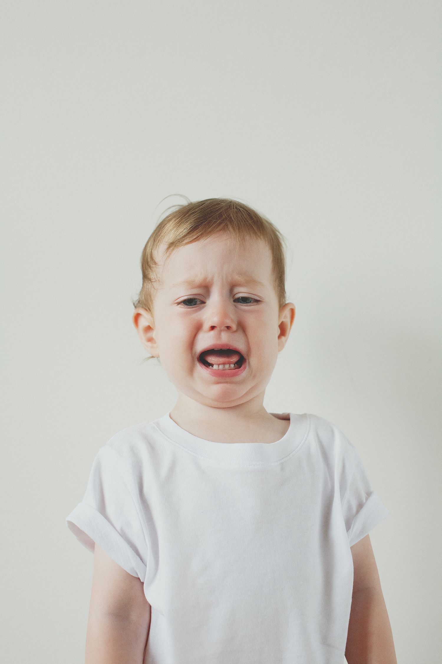 A toddler in a white t-shirt makes silly expressions against a light background.
