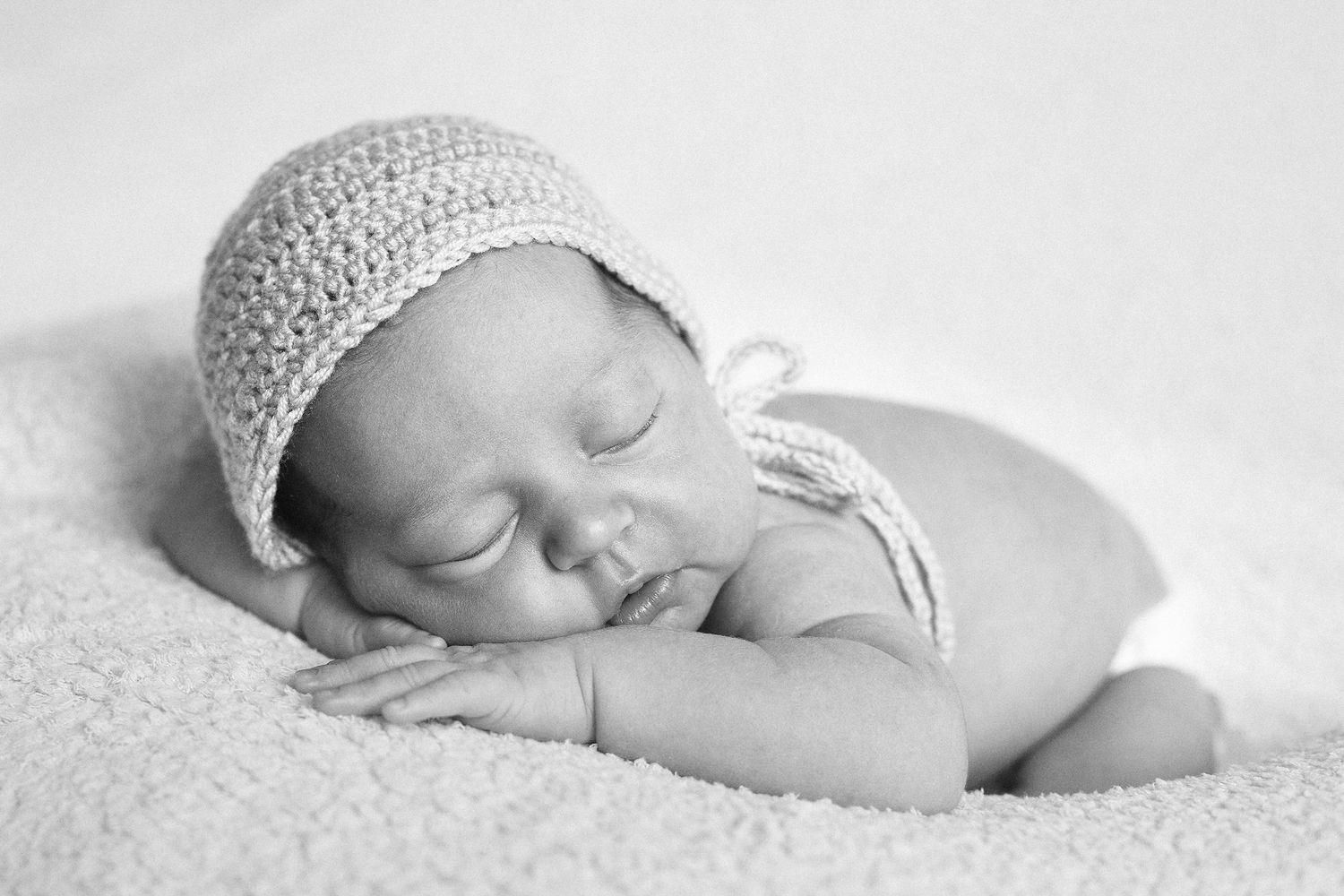 Sleeping newborn wearing knit hat in minimalist black and white portrait.