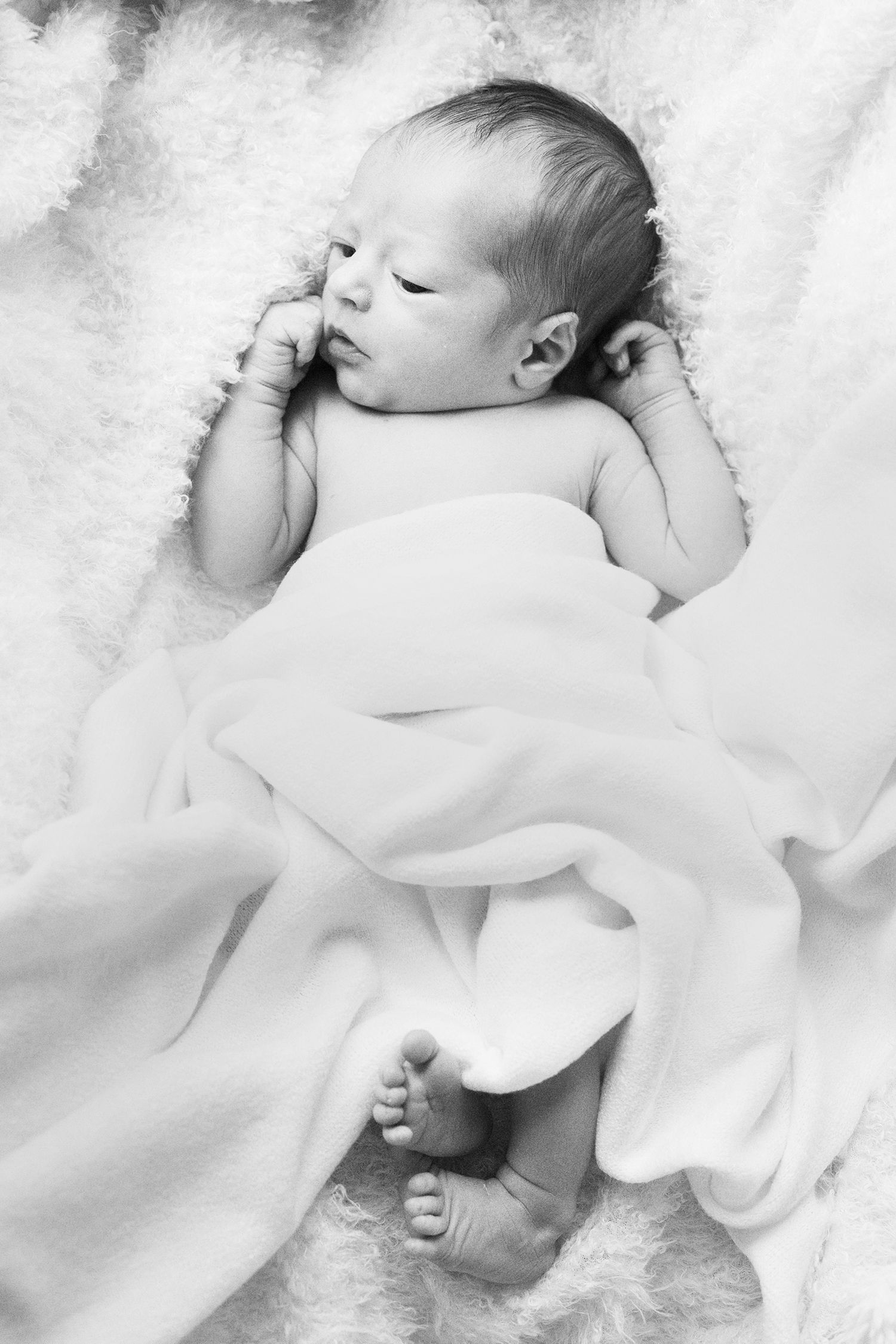 Sleeping newborn wrapped in soft white fabric against white background.