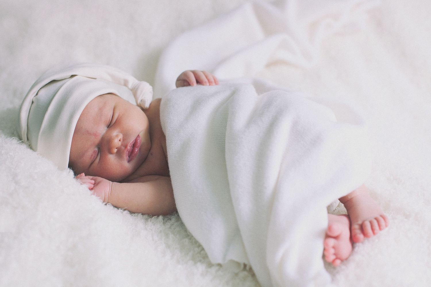 Peaceful sleeping newborn wrapped in soft white swaddle blanket.