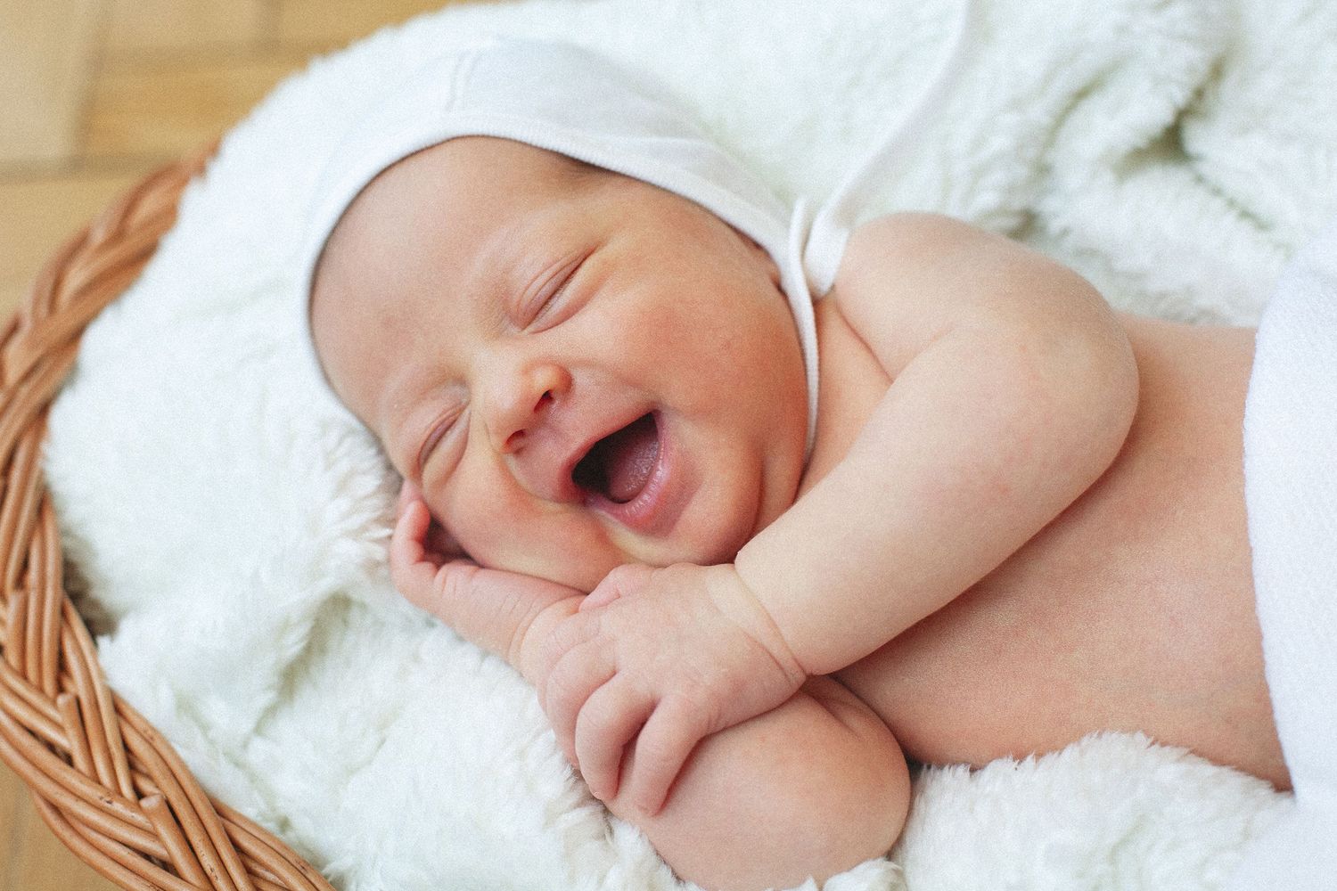 Newborn baby resting on soft white blanket in wicker basket.