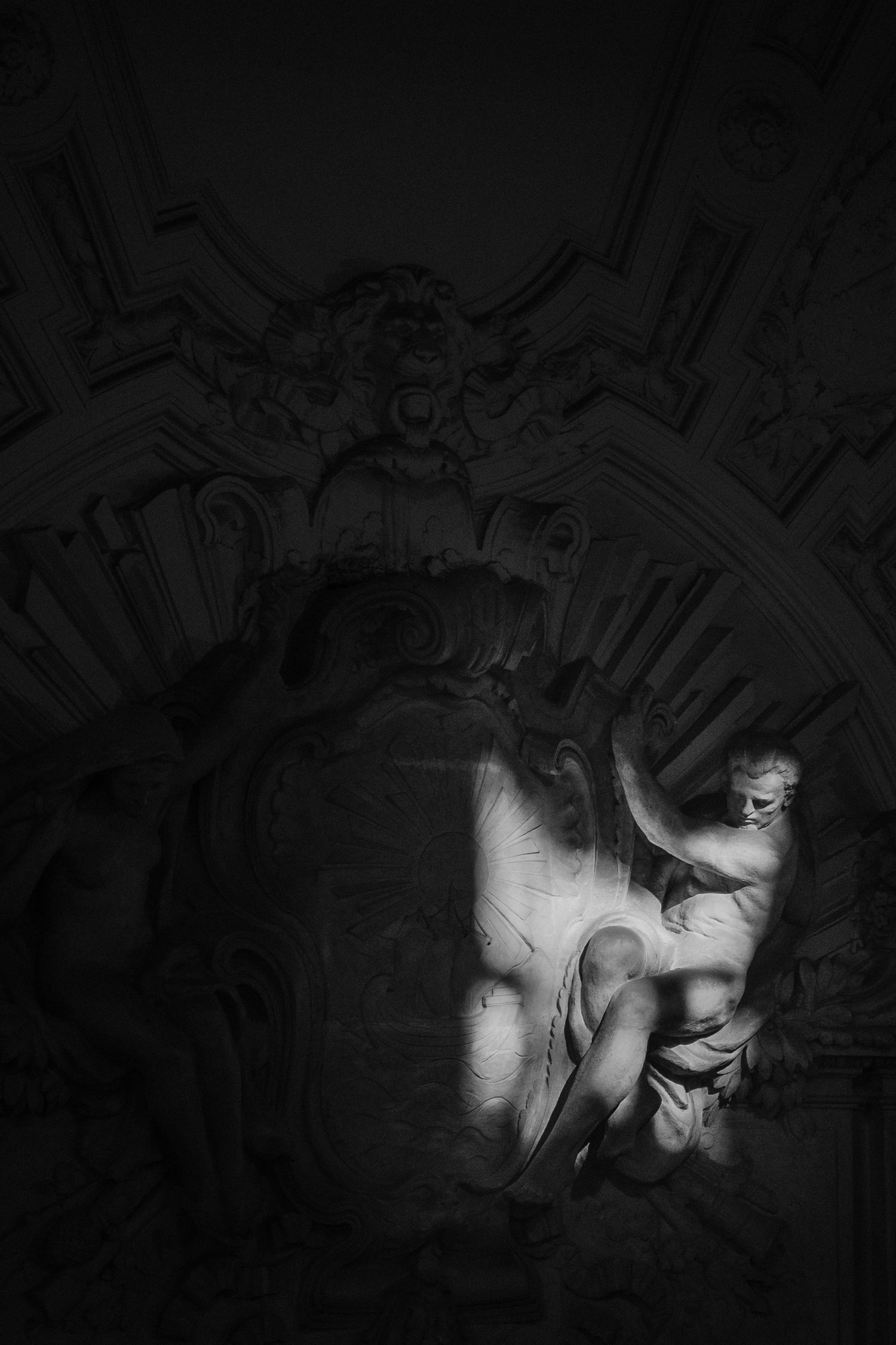 Marble sculpture in dramatic shadow, depicting a muscular figure amid ornate baroque architecture in black and white inside City Hall.