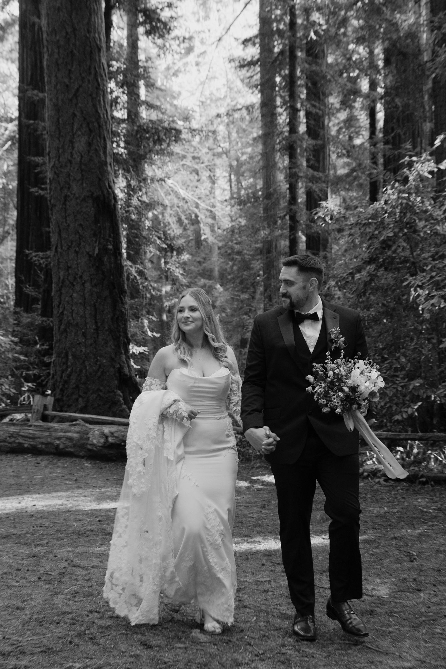 Bride and groom walking hand in hand through a redwood forest on their wedding day in black and white by Taylor Zimmerman Photo